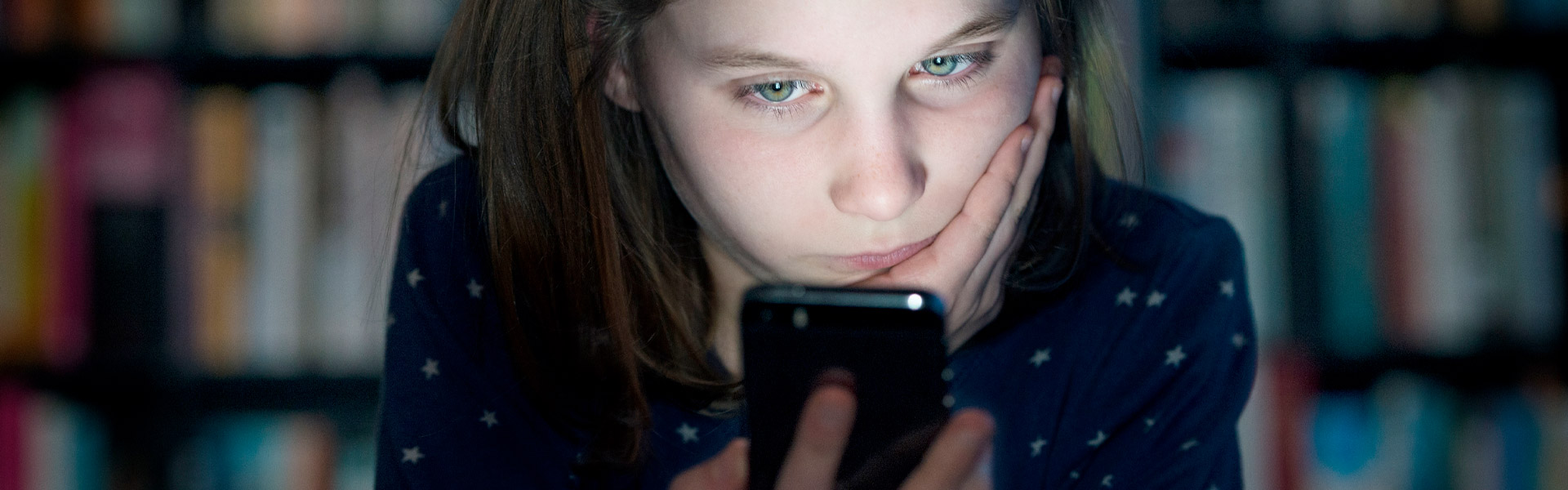 Mädchen blickt im Dunkeln traurig auf ihr Handy